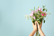 Female hands with bouquet of beautiful flowers on color background