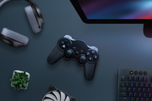 Joypad On Desk Surrounded With Headphones, Cooler, Keyboard And Computer Display. PC Gaming Concept. Top View, Flat Lay.