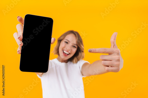 Fotografía Image of young blond woman pointing finger at smartphone in hand