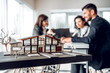 © HBS - Close up image of house model with group business people on blurred background in building design studio. Architecture project concept