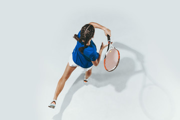 Young woman in blue shirt playing tennis. She hits the ball with a racket. Indoor studio shot isolated on white. Youth, flexibility, power and energy. Negative space. Top view.