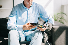 Cropped View Of Businessman Sitting On Sofa And Holding Plugged Router