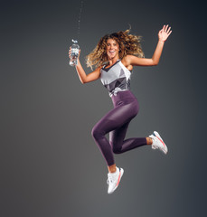 Happy joyful girl is jumping with bottle of water making splashes at photo studio on dark background.