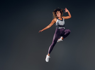 Happy attractive woman in activewear is jumping at studio over grey background.