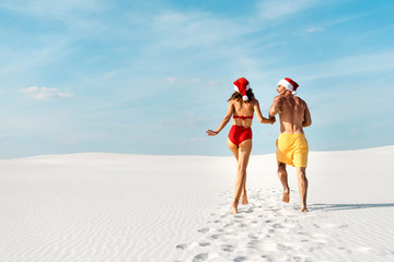 back view of sexy girlfriend and boyfriend in santa hats running on beach in Maldives