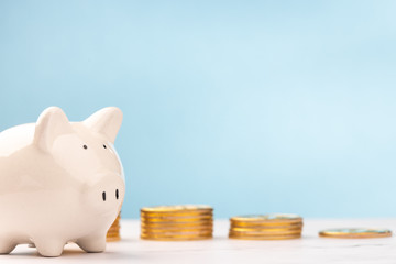 Cute piggy bank with gold coins on white table and blue background. savings money concept.