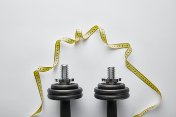 top view of heavy black dumbbells near yellow measuring tape on white