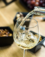 Wall Mural - Pouring white wine into the glass against wooden table