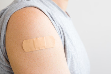 brown adhesive bandage on young man's arm after scratch on skin or injection of vaccine. first aid. 