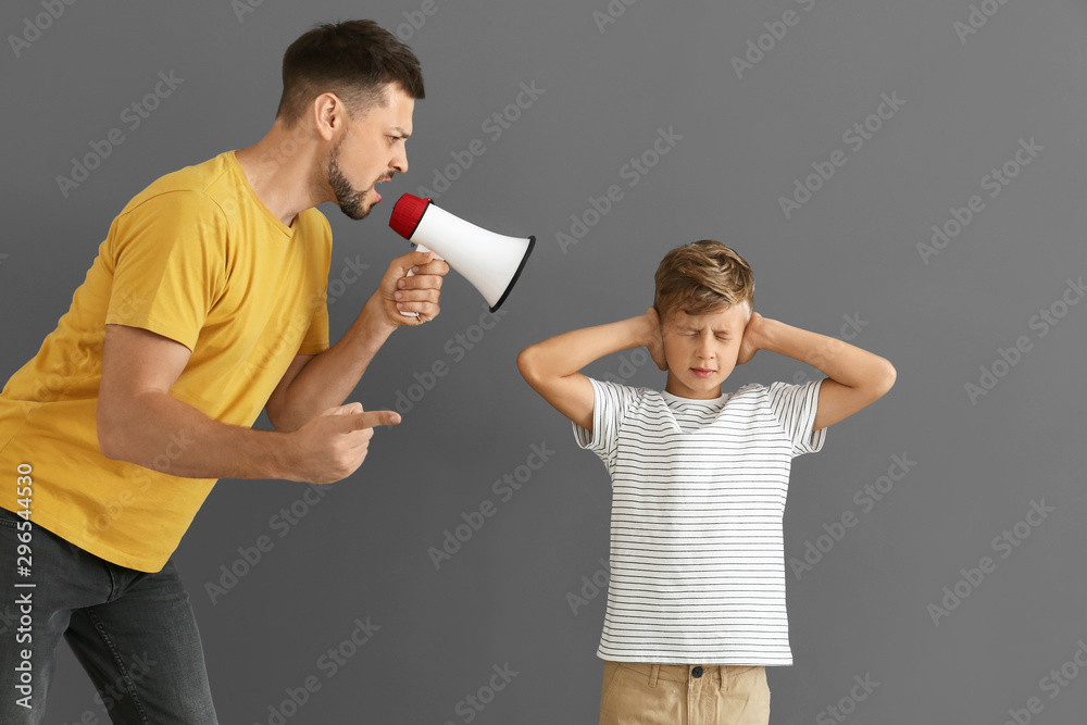 Little boy ignoring his angry father with megaphone against grey background