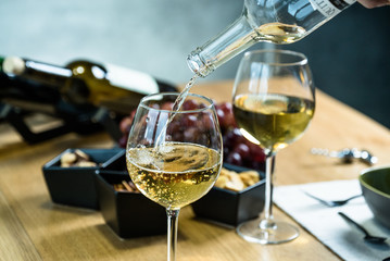 Wall Mural - Pouring white wine into the glass against wooden table