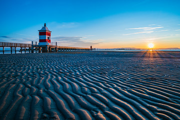 Sunrise over the sea. The lighthouse of Lignano Sabbiadoro and the games of sand and colors. Italy