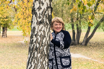 Autumn.  A young, cheerful woman is standing by a white birch.