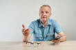 © amixstudio - Authentic photo portrait of elderly talking man sitting at table with mobile phone in hand, modern advanced candid senior citizen on white background