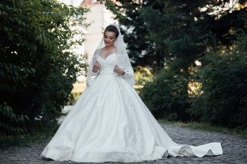 Attractive young bride in white dress with train. Beautiful bride outdoor. Fashion, beauty, style. Wedding photography.  Beautiful bride with make up and hair style.