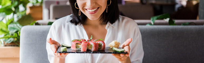 Wall Mural - panoramic shot of happy woman holding plate with tasty sushi