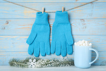 Knitted Mittens With Fir Tree Branches And Cup Of Drink On Blue Wooden Background