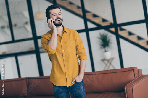 Photo of handsome guy holding hands in pockets easy-going person speaking over telephone with partner about startup investment in modern trendy interior flat indoors