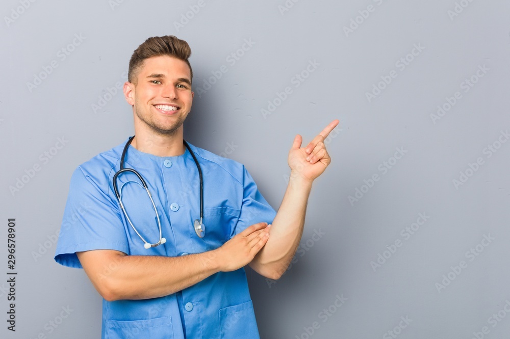 Young nurse man smiling cheerfully pointing with forefinger away. - obrazy, fototapety, plakaty 