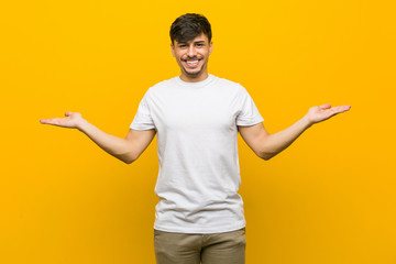 Young hispanic casual man makes scale with arms, feels happy and confident.