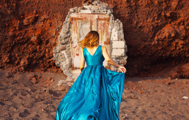 Young beautiful woman in blue dress walking on the beach at Santorini.