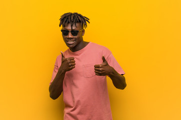 Wall Mural - Young casual black man wearing sunglasses raising both thumbs up, smiling and confident.