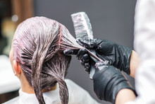 Close Up Back View Of Hairdresser Is Applying Color To Customer's Hair In Black Gloves. Hair Coloring In A Beauty Salon. Beauty And People Concept.