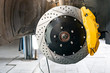 The braking system of the car with the wheel removed with the disc, pads, yellow hub and cooling holes during maintenance and replacement in the workshop on the vehicle repair. Auto service industry.