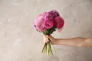 Woman holding bouquet of beautiful aster flowers on beige background, closeup