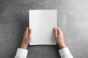 Man holding blank booklet at grey table, top view. Mock up for design