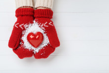 Hands In Knitted Mittens Holding Red Heart On White Wooden Table