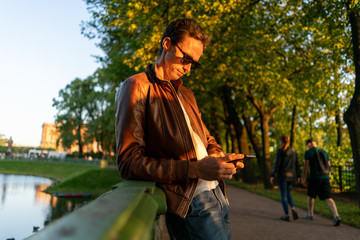 guy is looking at a smartphone. in the park in the light of the setting sun in sunglasses