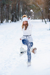 Wall Mural - Beautiful young woman weared in white sweater and hat with ice skates on the hands having fun in winter snowy park.