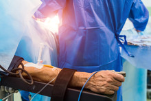 Restrainted Patient On The Operation Table In Surgery With A Drip In A Hand. Patient's Hand With A Sensor,Hand Critically Ill Patients. IV Fluids. Closeup.