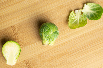 Group of one whole one half two pieces of fresh green brussels sprout flatlay on light wood