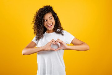 happy beautiful black girl showing heart with hands isolated over yellow