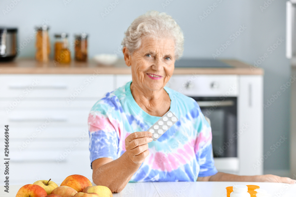 Elderly woman with pills at table in kitchen