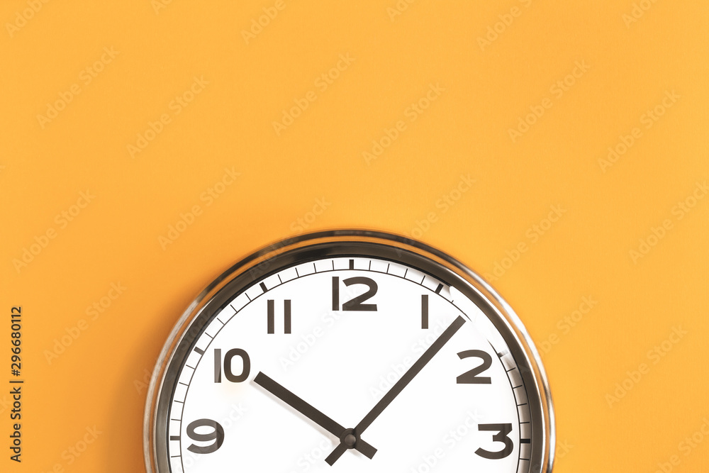 Part of analogue plain wall clock on trendy pastel orange background. Ten o'clock. Close up with copy space, time management or school concept and summer or winter time change - obrazy, fototapety, plakaty 