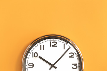 part of analogue plain wall clock on trendy pastel orange background. ten o'clock. close up with cop