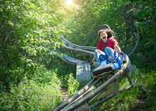 Screaming Teen Girl Riding Downhill On An Outdoor Roller Coaster On A Warm Summer Day. She Has A Fun Expression On Her Face As She Enjoys A Thrilling Ride On An Amusement Park Ride