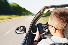 Closeup Of Man Using A Smartphone While Driving A Car. Driving Into Oncoming Traffic. Dangerous Movement. Distracted By Phone. The Guy Writes A Message In Phone While Driving. Effect Blurred Motion
