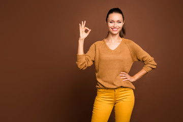 Photo of cheerful confident attractive youngster holding hand on waist showing you ok sign wearing brown sweater isolated over brown color pastel background