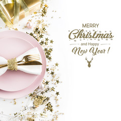 Christmas table setting with pink dishware, golden silverware and party decorations on white background. Top view. Xmas invitation.