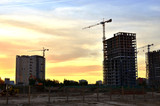 Fototapeta Miasto - Jib construction tower crane and new residential buildings at a construction site on the sunset and blue sky background - Image
