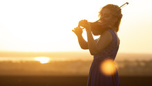 Silhouette Of A Female Figure Playing The Vio And Hobbylin At Sunset, Woman Relaxing In Music, Performance On Nature, Concept Art