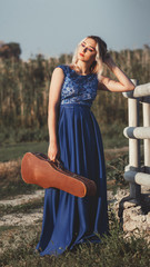 Wall Mural - portrait of a beautiful girl in a long dress with a violin near a wooden painted fence, a young woman walks with a musical instrument outdoors