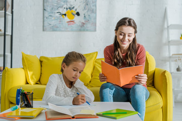 selective focus of attractive babysitter holding notebook near cute child studying at home