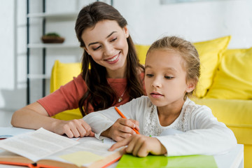 Wall Mural - selective focus of cute kid pointing with finger at book near cheerful babysitter at home