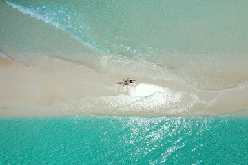 Wall Mural - romantic couple stretched on the white sand of a maldivian beach from aerial view