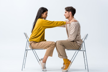 Wall Mural - side view of attractive girl sitting on chair and touching man on white